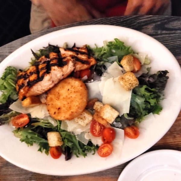 Grilled salmon and a fried risotto ball on a bed of greens with cherry tomatoes and croutons.