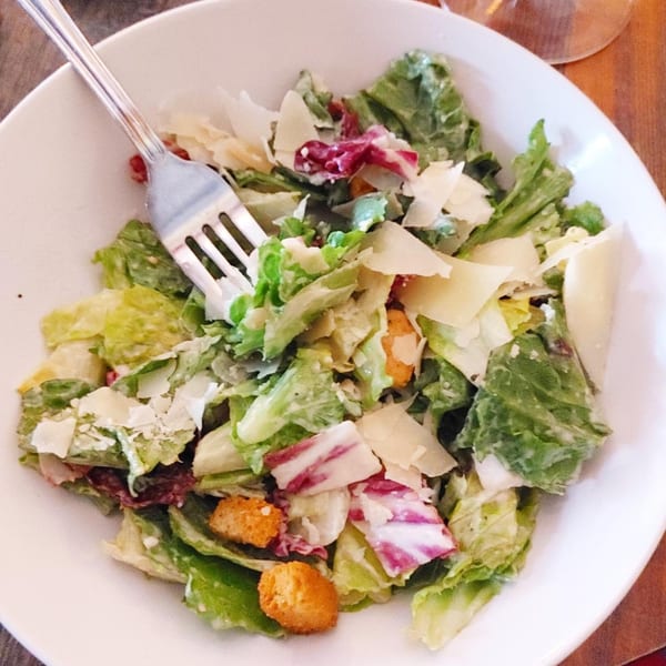 A Pignetti's Italian restaurant Caesar salad with parmesan, croutons, and radicchio in a white bowl.