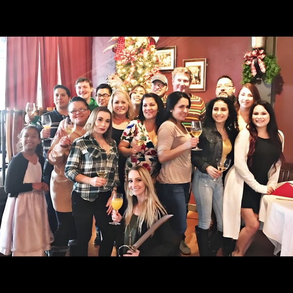 A large group of people celebrating with drinks in a festive, Italian restaurant setting.