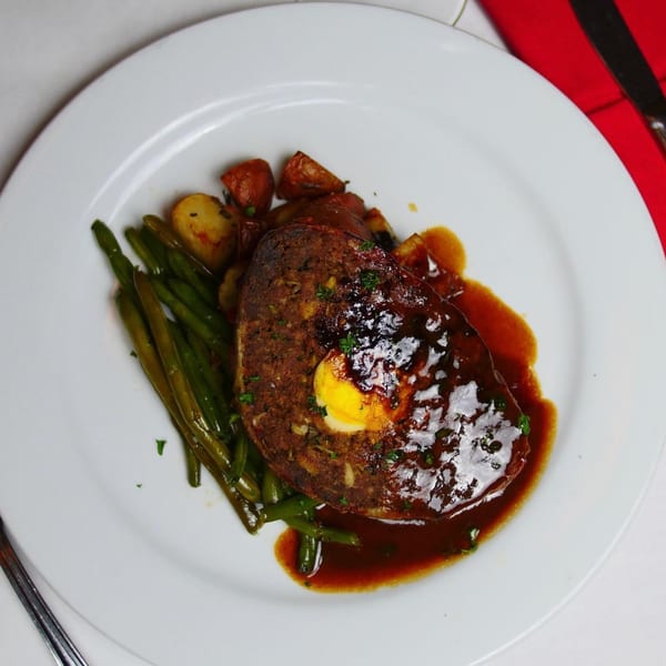 Meatloaf with a hard-boiled egg center, green beans, and roasted potatoes on a white plate.
