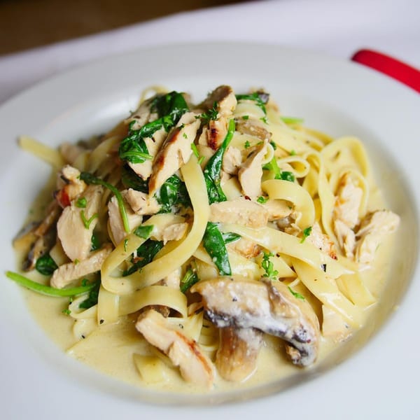 Pignetti's creamy fettuccine pasta with chicken, spinach, and mushrooms on a white plate.
