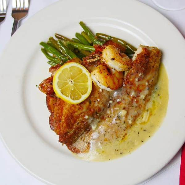 Pignetti's Italian dish with pan-seared fish, shrimp, green beans, lemon slice, and creamy sauce.
