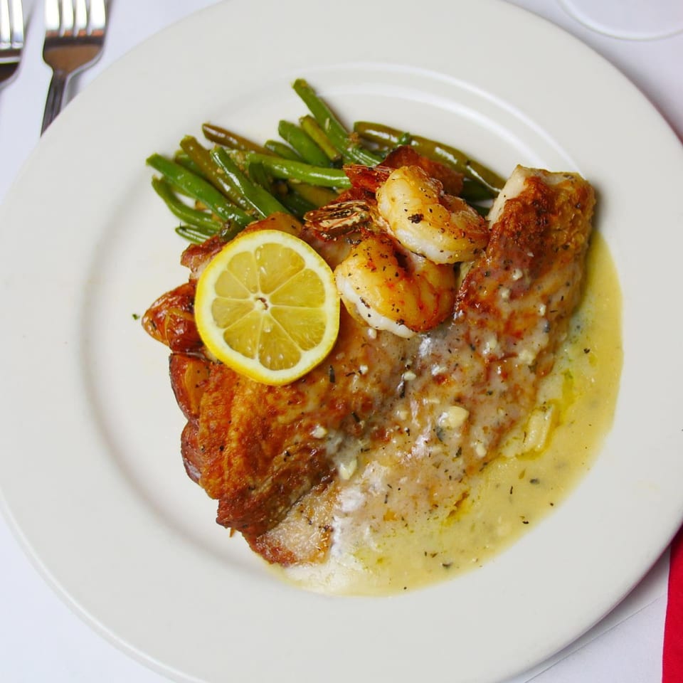 Pignetti's Italian dish with pan-seared fish, shrimp, green beans, lemon slice, and creamy sauce.