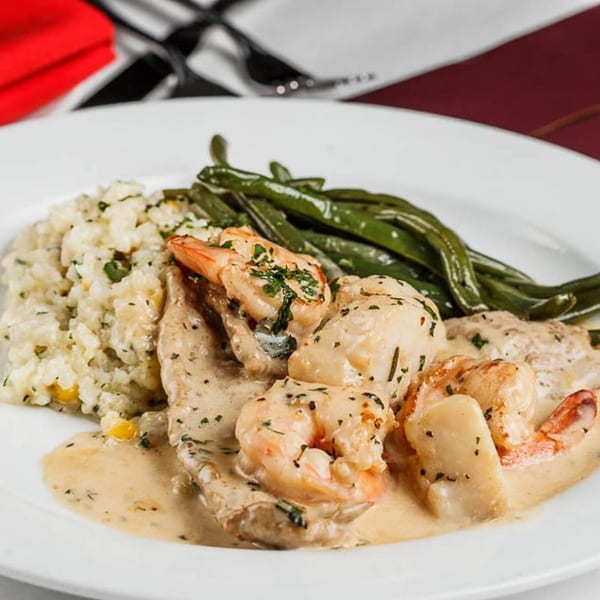 Pignetti's creamy shrimp and scallops with risotto and green beans on a white plate.