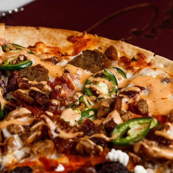 Close-up of a Pignetti's pizza with meat, jalapeños, and a creamy sauce.