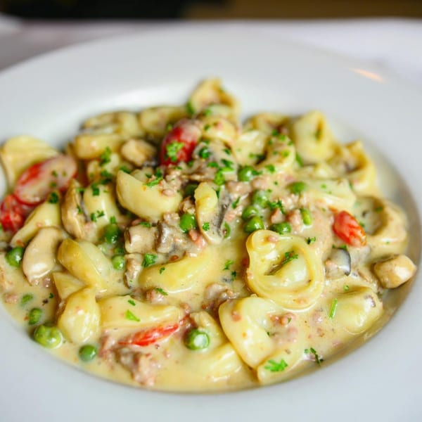 Pignetti's creamy tortellini pasta with peas, mushrooms, and diced tomatoes on a white plate.
