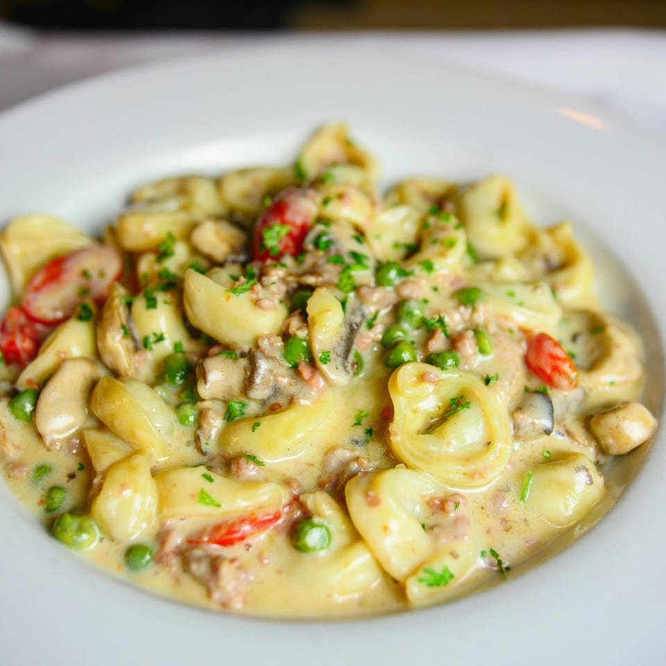 Pignetti's creamy tortellini pasta with peas, mushrooms, and diced tomatoes on a white plate.