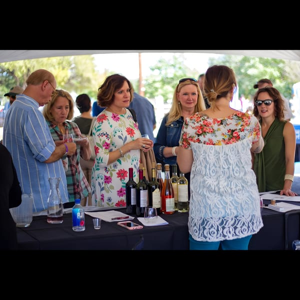 Guests gather around a table with wine bottles, enjoying drinks at an outdoor Pignetti's event.