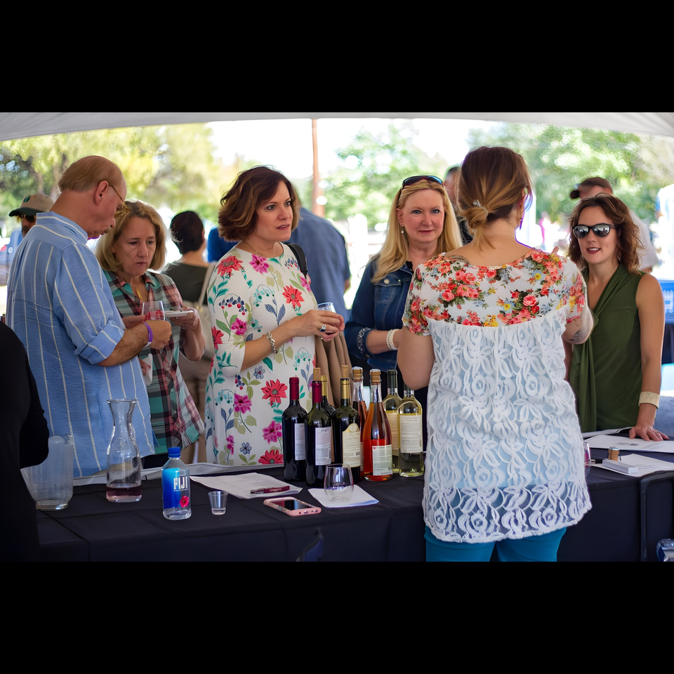 Guests gather around a table with wine bottles, enjoying drinks at an outdoor Pignetti's event.
