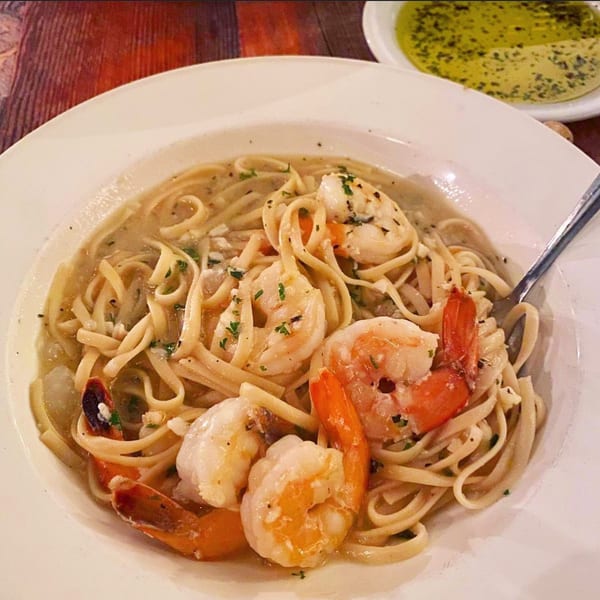 Pignetti's shrimp scampi with linguine pasta in a white bowl, with a side of olive oil.
