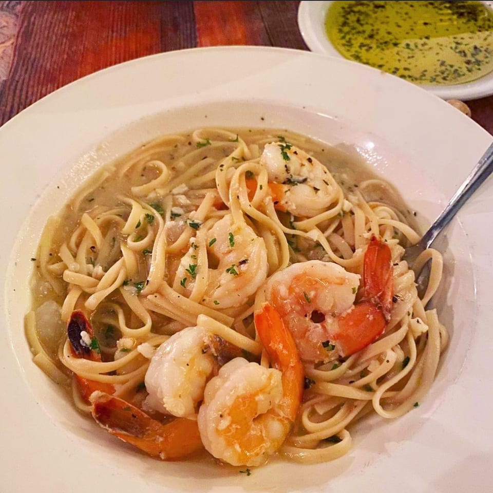 Pignetti's shrimp scampi with linguine pasta in a white bowl, with a side of olive oil.