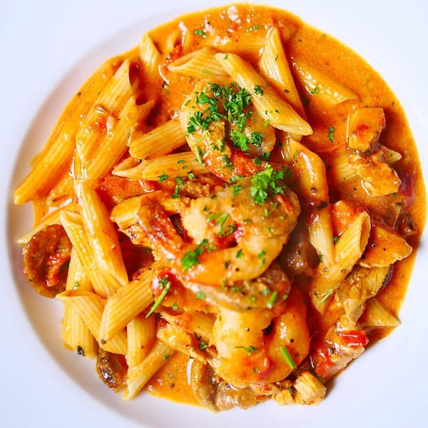 Pignetti's penne pasta with shrimp, chicken, and mushrooms in a creamy tomato sauce, garnished with parsley.
